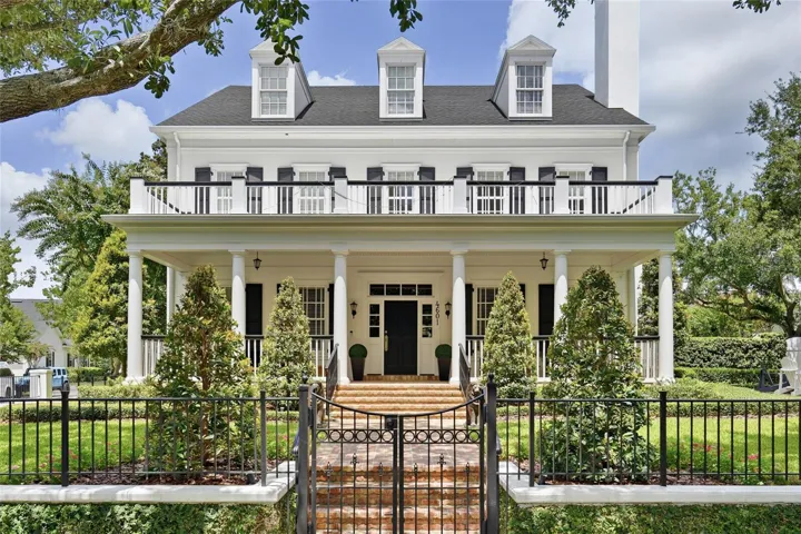 A striking front elevation showcases the home’s symmetrical design, expansive covered porch, upper balcony and beautifully manicured landscaping.