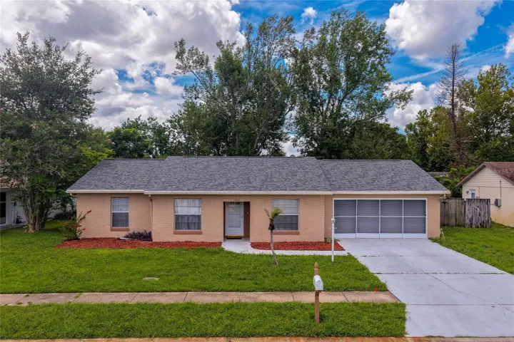 Charming single-story home featuring a spacious front lawn, concrete driveway, and screened garage enclosure. Lush surrounding trees and vibrant landscaping complete the inviting curb appeal.