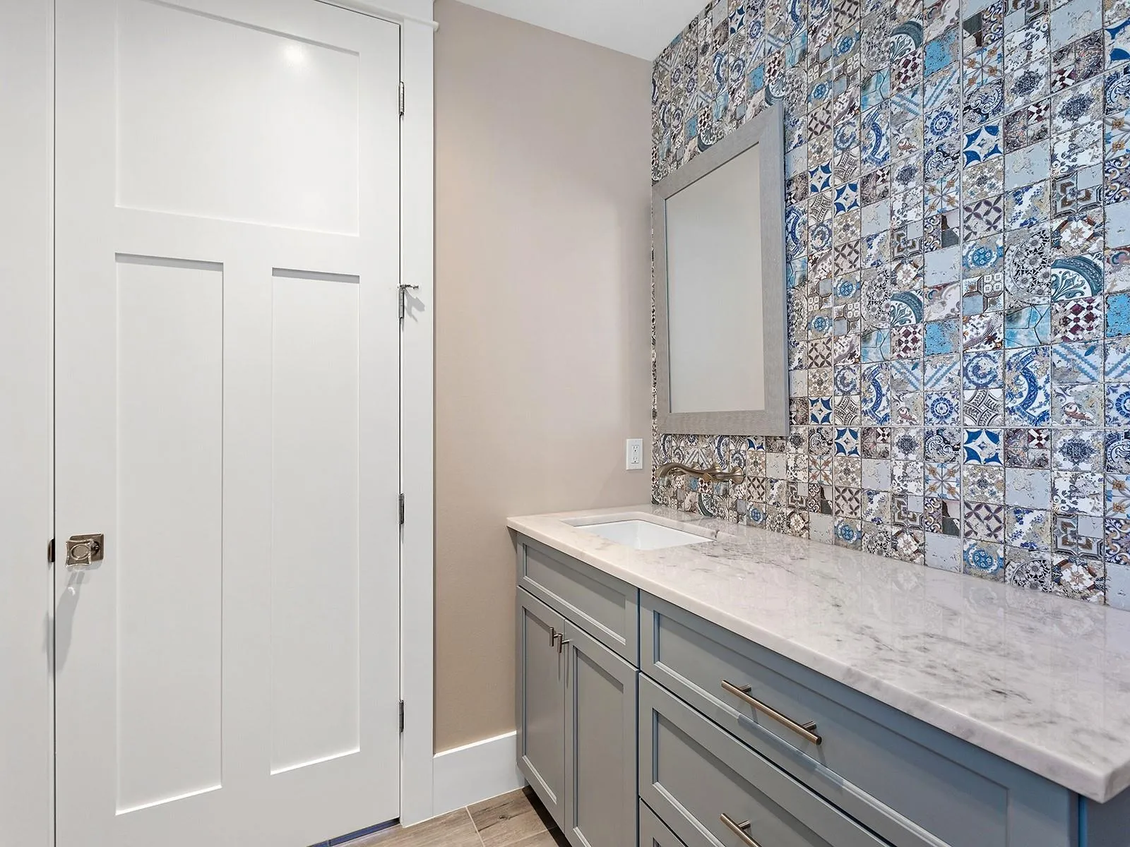 Half bath on the ground floor. Mediterranean-inspired mosaic tile feature wall, brushed gold wall-mounted hardware, and light quartz countertops