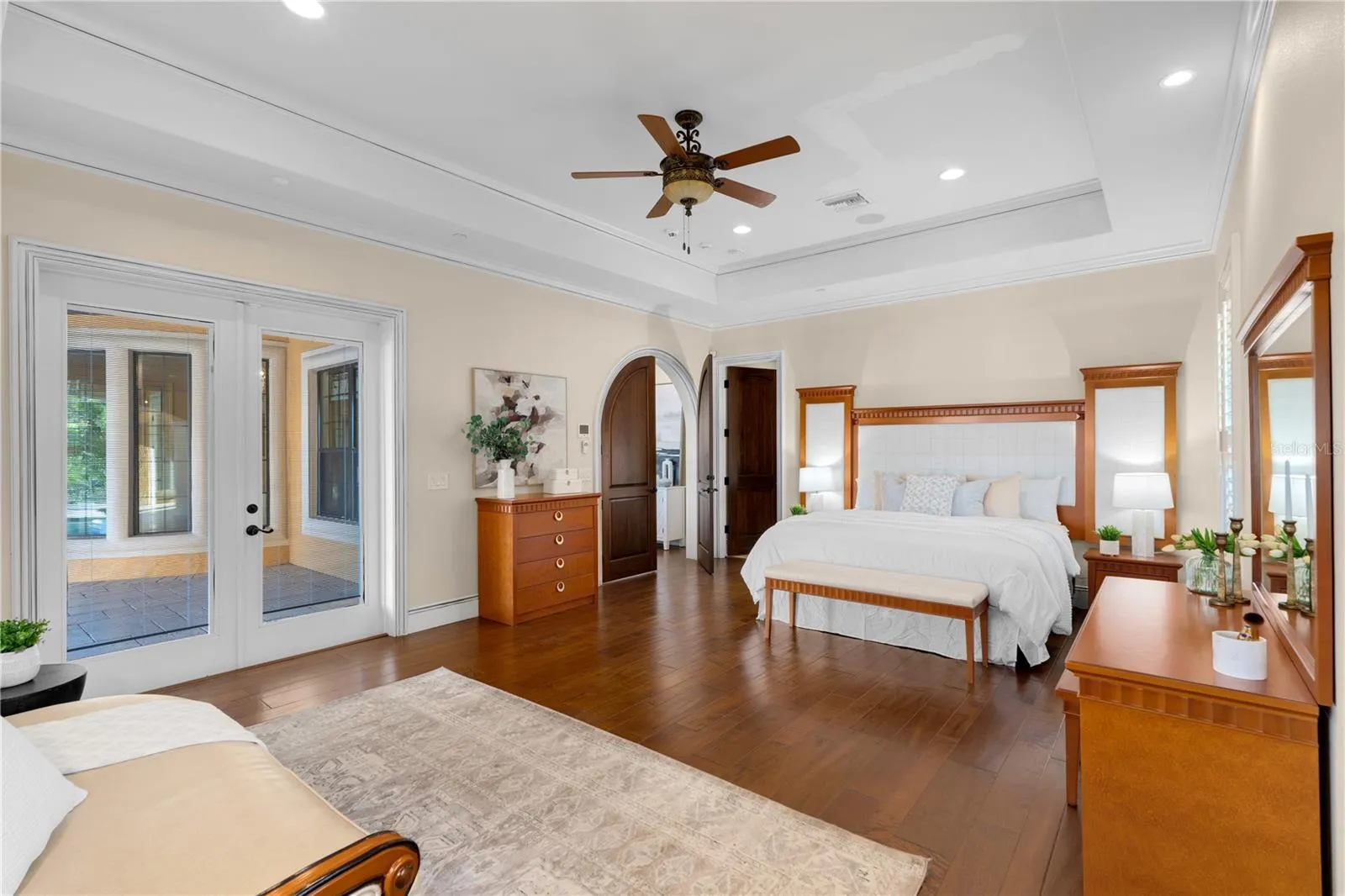A serene first-floor primary bedroom offers rich hardwood flooring, a tray ceiling and abundant natural light within this Lake Mary waterfront residence.