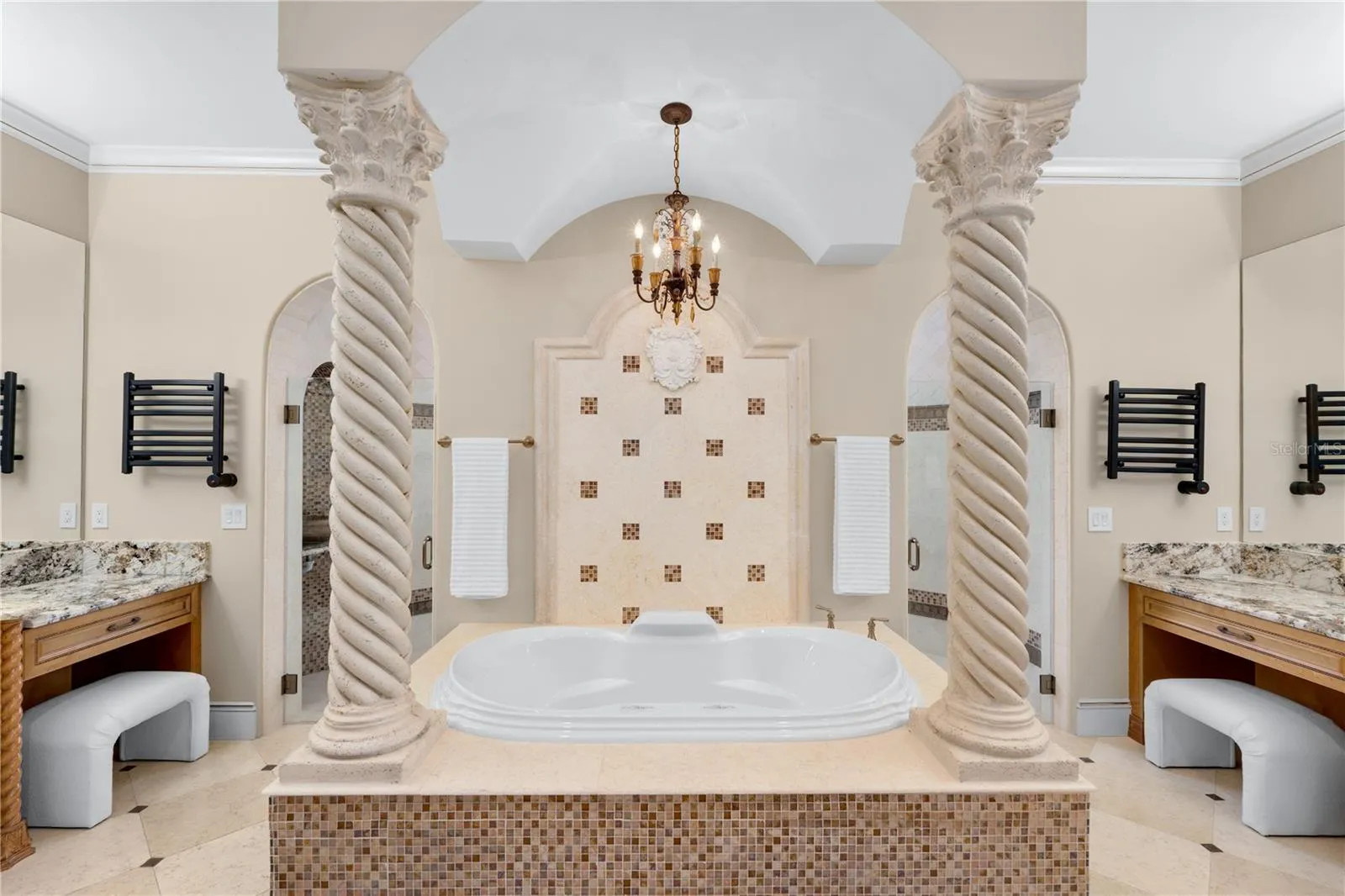A spa-inspired primary bath is centered around an elevated Jacuzzi soaking tub framed by decorative columns and beautifully appointed dual vanity areas.