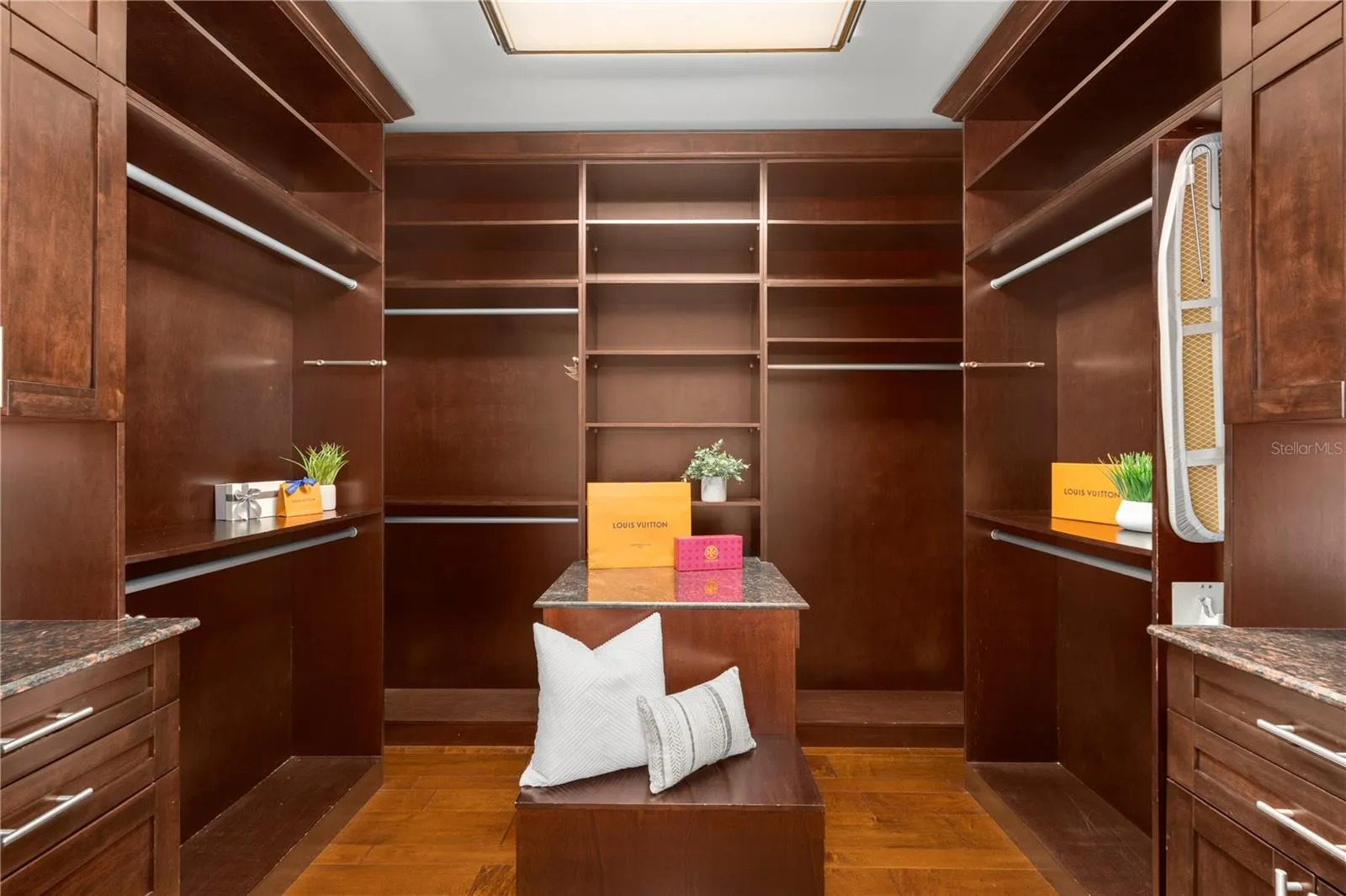 A bespoke walk-in wardrobe is finished in rich custom wood cabinetry with extensive hanging areas, shelving, drawers and thoughtfully designed storage.
