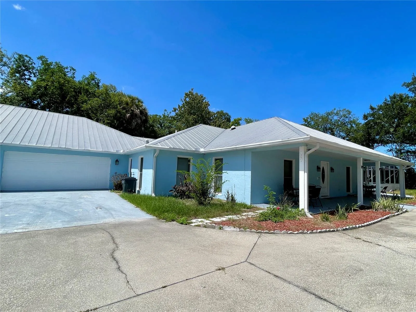 Welcoming exterior view featuring a light coastal-inspired color palette, metal roof attached garage, covered entry, and an expansive paved approach.