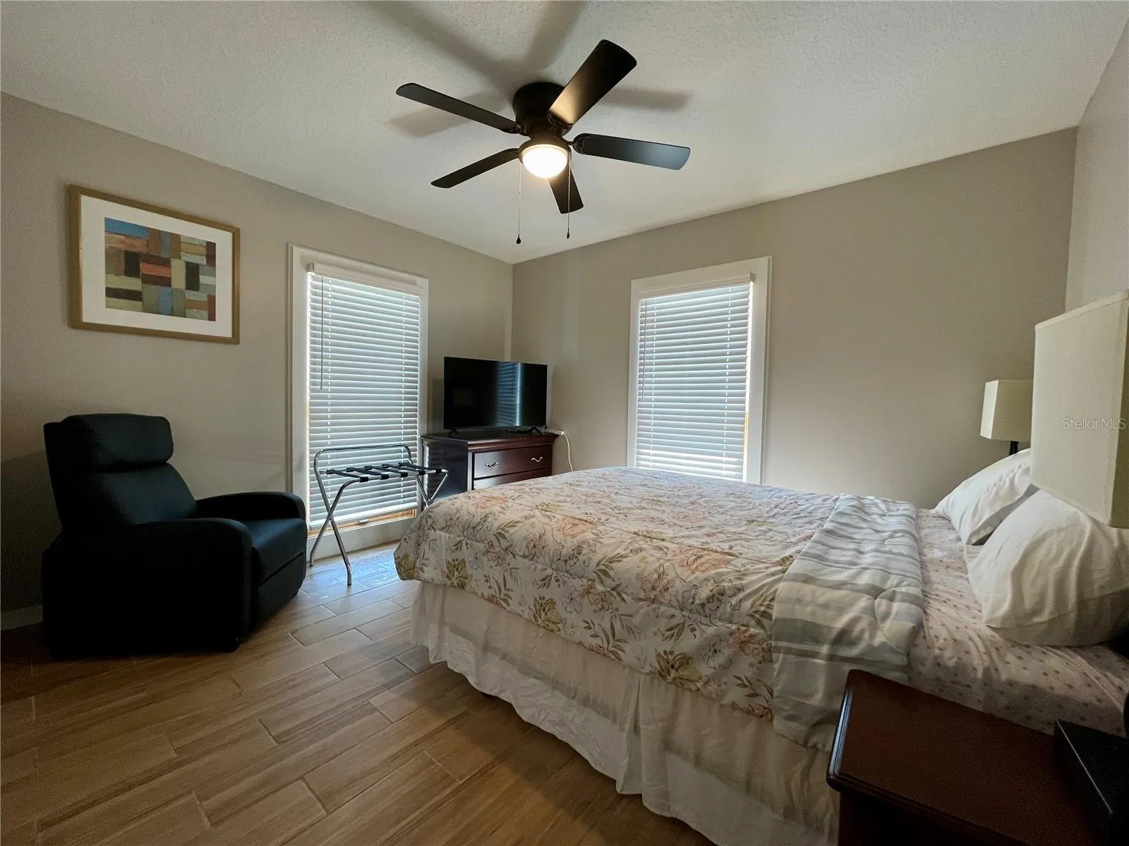 Bright bedroom offers two tall windows, neutral finishes, and a ceiling fan, with ample space for additional furnishings.