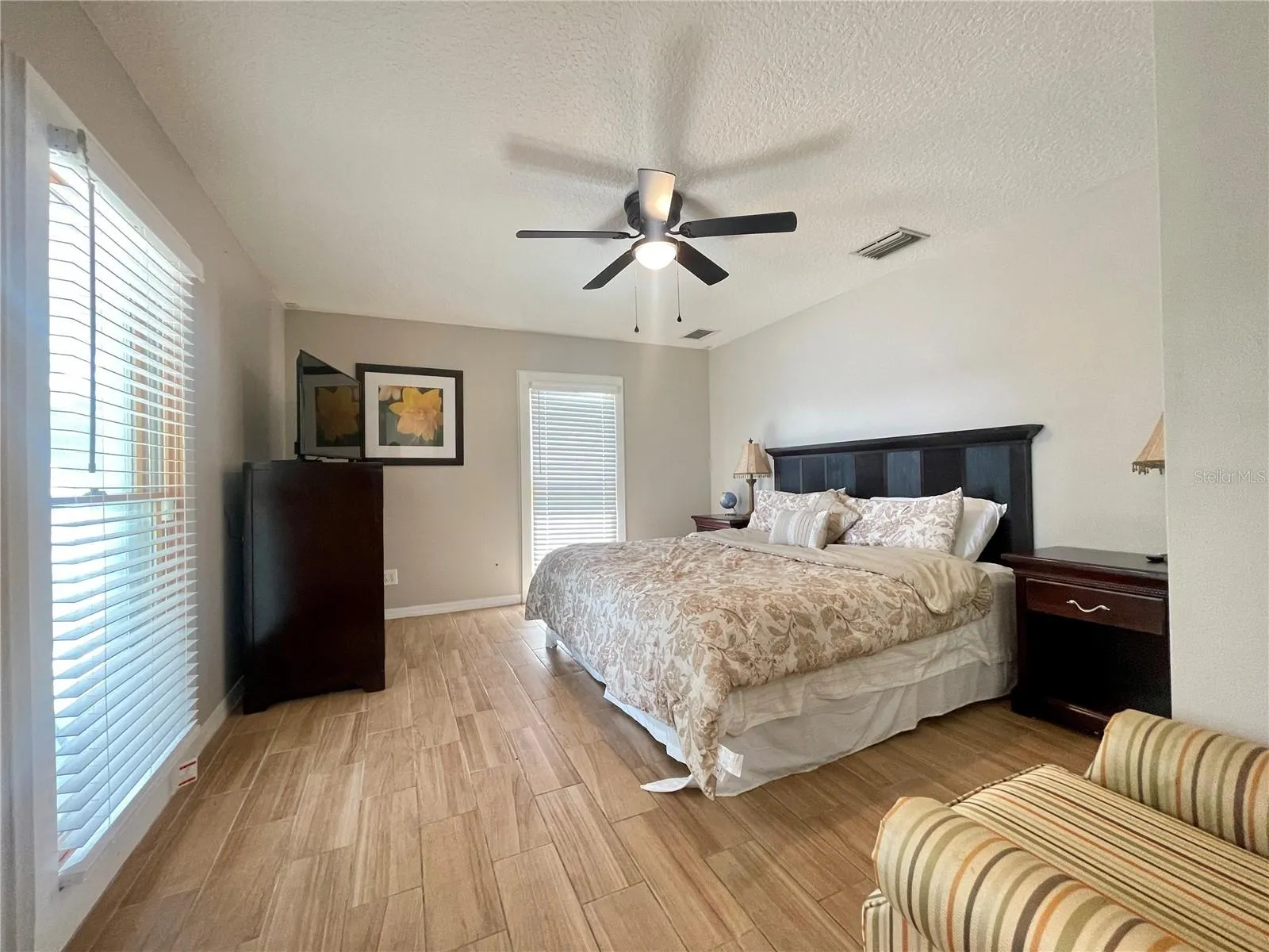Comfortable bedroom with abundant natural light from multiple windows, neutral finishes, and a ceiling fan with light.