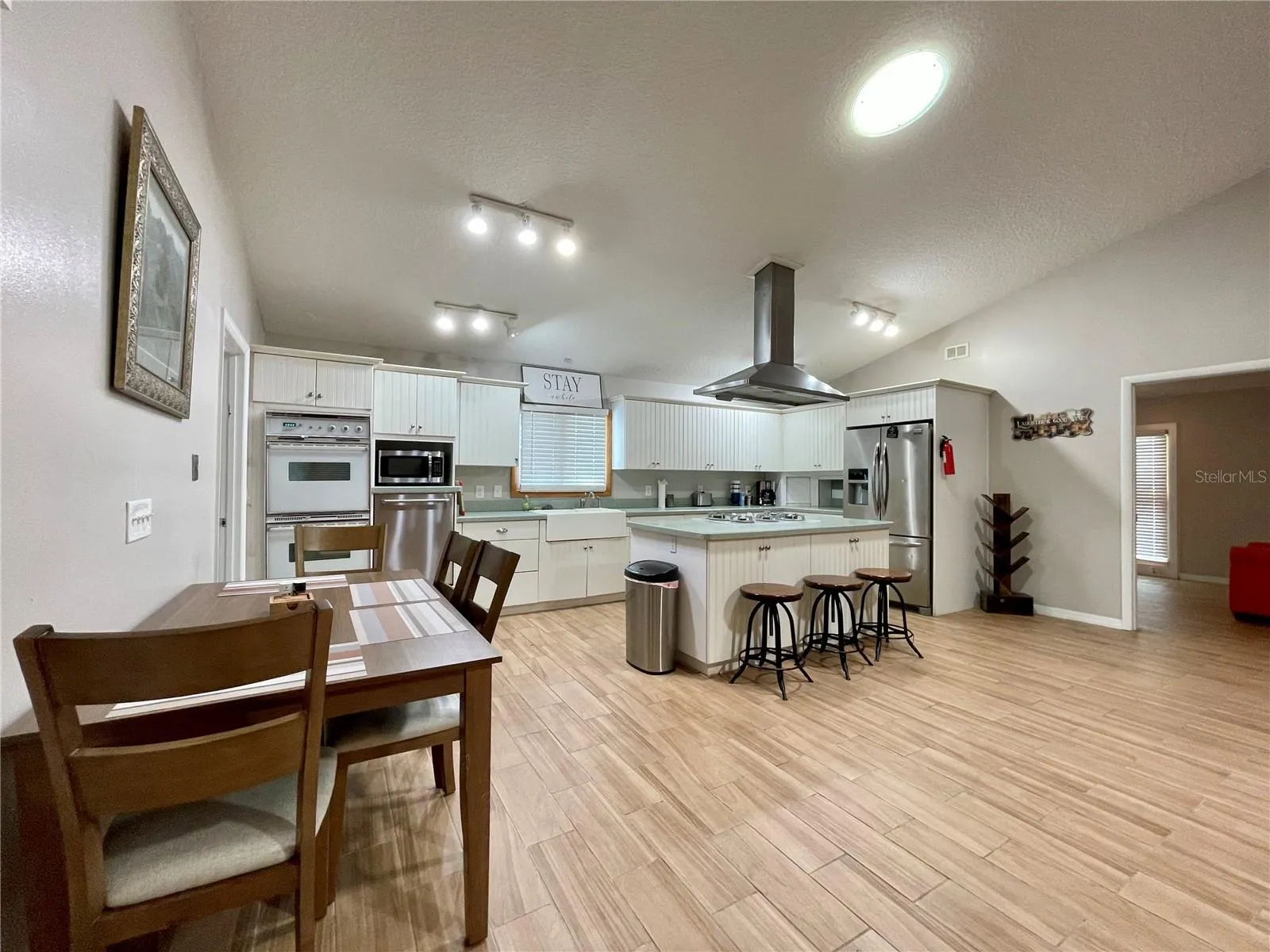 Spacious kitchen offers abundant cabinetry and counter space, stainless steel appliances, a center island with seating, and an adjoining dining area beneath the open ceiling.