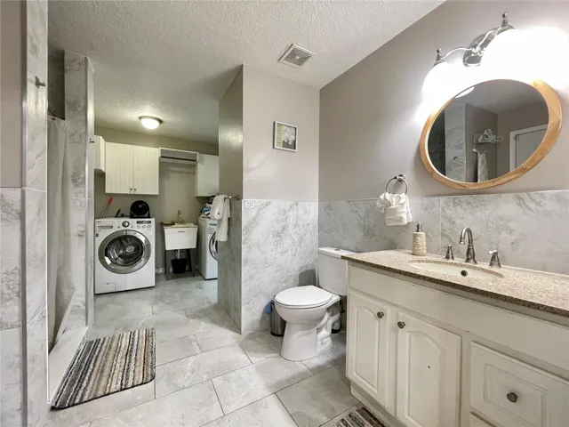 Versatile bathroom features a vanity, tiled finishes, and convenient direct access to the adjoining laundry area.