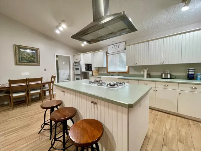 The center island provides additional prep space, a built-in cooktop, casual seating, and a contemporary stainless steel range hood, with extensive cabinetry surrounding the workspace.