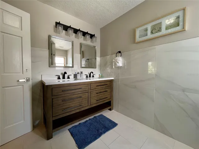 Updated bathroom features a double-sink vanity with contemporary black fixtures, dual mirrors, decorative lighting, and large-format wall tile.
