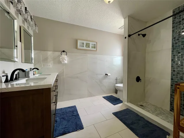 Updated bathroom offers a double-sink vanity, large-format wall tile, contemporary black fixtures, and a spacious tiled walk-in shower with mosaic detailing.