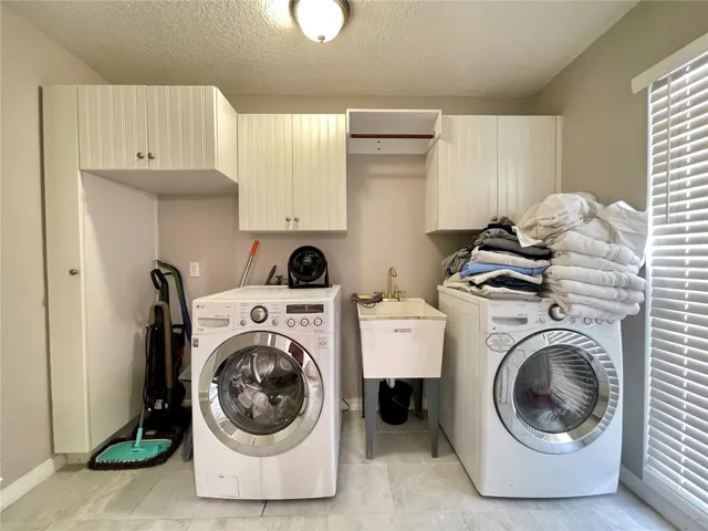 Dedicated laundry space offers upper cabinetry for storage, a utility sink, room for full-size appliances, and natural light from a window.