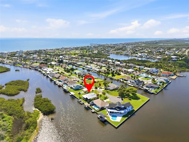 Aerial view — Aerial view of the canal-front property showing direct water access to the Intracoastal Waterway, with two covered boat lift areas on the dock, a backyard pool, detached garage, and mature palm landscaping