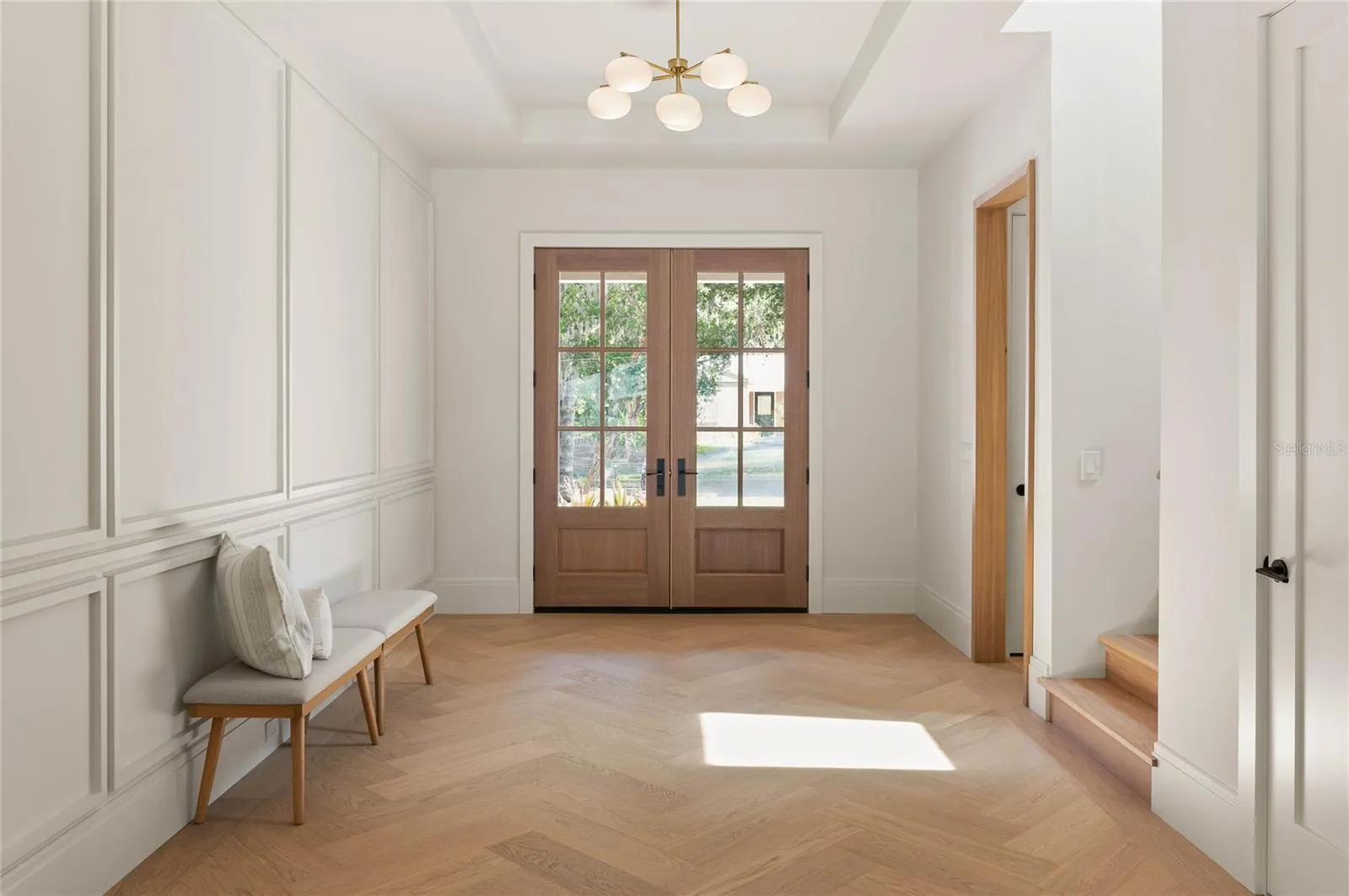 Welcoming foyer features custom herringbone-pattern white oak flooring, a tailored accent wall and white oak-cased openings