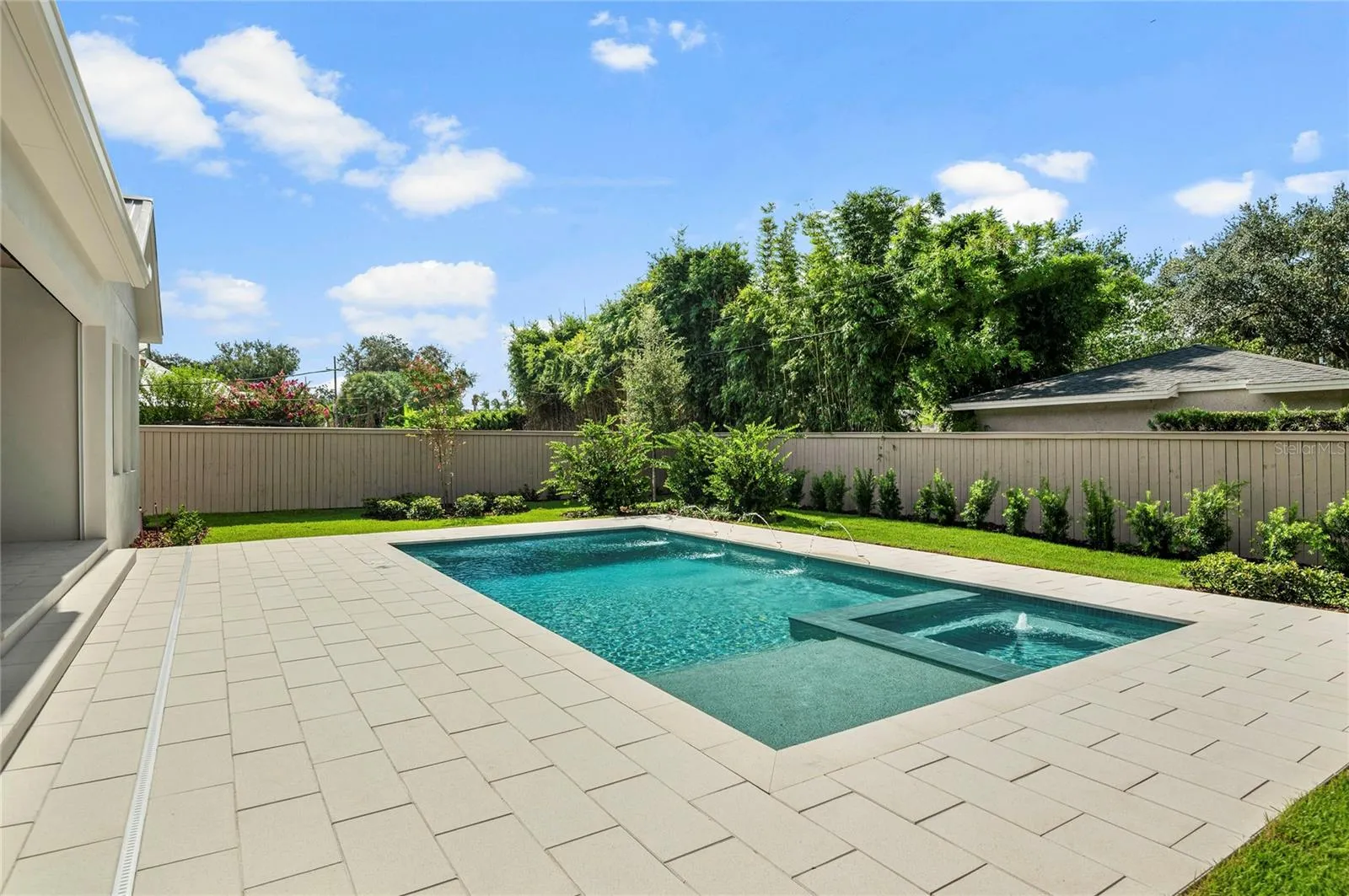 Artistic Paver decking surrounded by meticulously landscaped backyard with custom fencing