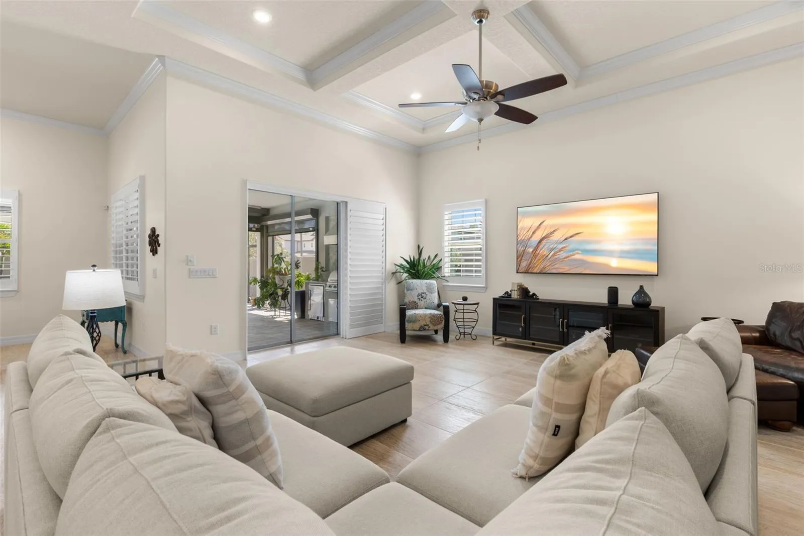 A soft, neutral color palette keeps the great room feeling light and inviting, while the dramatic tray ceiling, ceiling fan and plantation shutters add polished detail. Wide sliding glass doors create an easy connection to the screened lanai and pool.