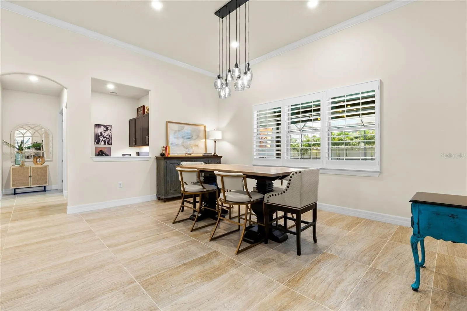The dining area feels open and gracious, with oversized tile flooring, crown molding, plantation shutters and a striking clustered-glass chandelier overhead.