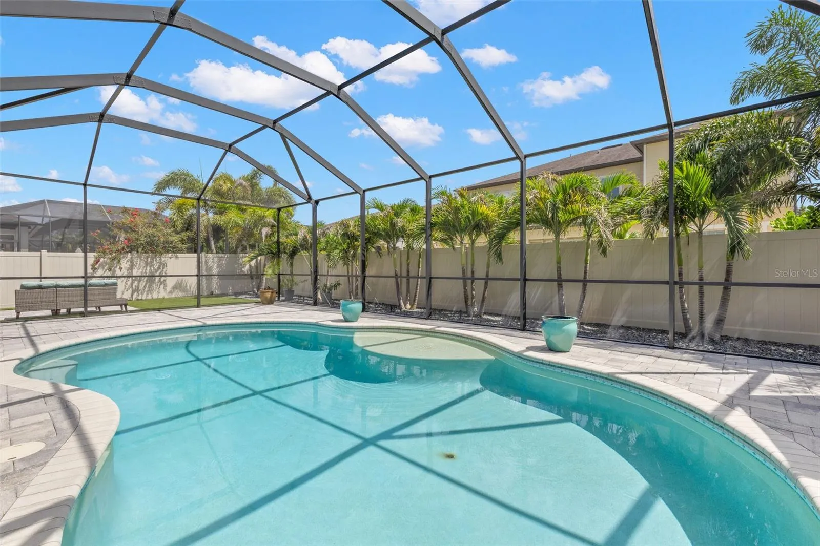 A row of lighted palms creates a lush tropical backdrop around the screened pool, adding privacy by day and taking on a whole new look after dark with landscape lighting. The sun shelf offers an easy place to cool off without leaving the water.