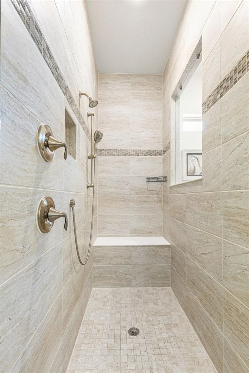 The oversized walk-in shower is finished from floor to ceiling in coordinating tile, with a built-in bench, recessed niche, decorative accent band, fixed showerhead and handheld spray, a spacious, thoughtfully designed complement to the primary bath.