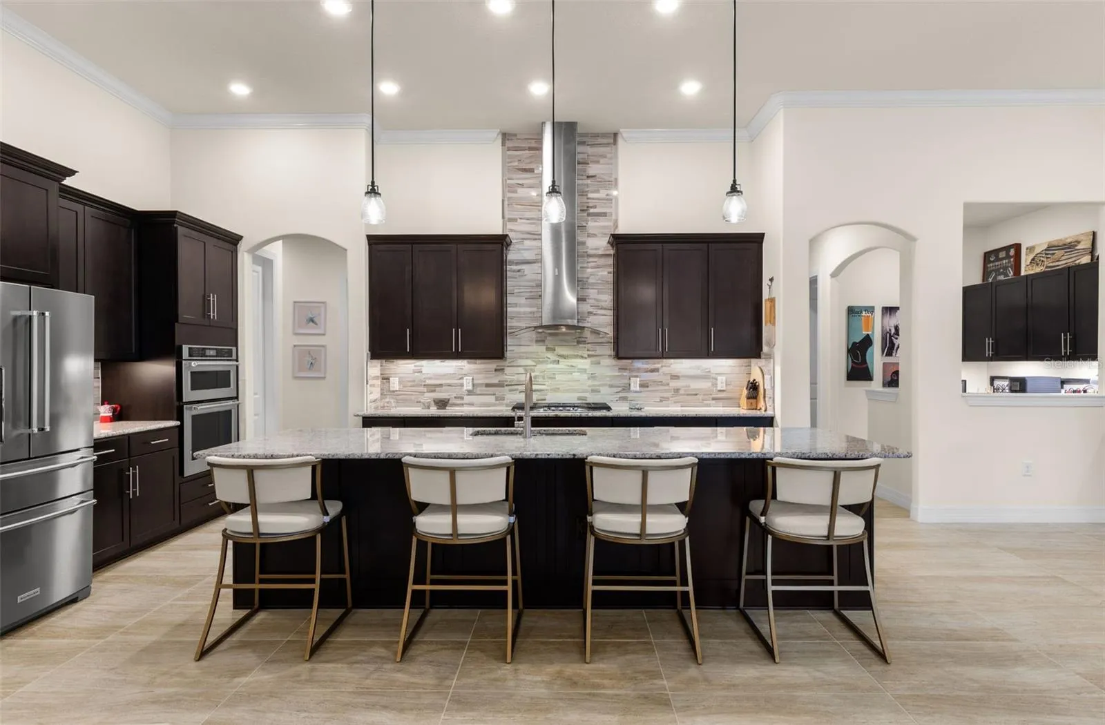 The kitchen is built to be used and enjoyed, with a generous granite-topped island offering seating for four, rich cabinetry, double ovens and a gas cooktop beneath a striking stainless hood and full-height tile backsplash. Pendant and recessed lighting keep the space bright, while the open design makes it easy to stay connected to the living and dining areas.