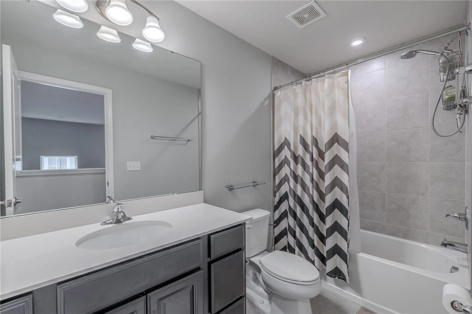 The second full bath combines a spacious single-sink vanity, oversized mirror and neutral finishes with a tiled tub-and-shower combination, creating a bright, functional space for family or guests.