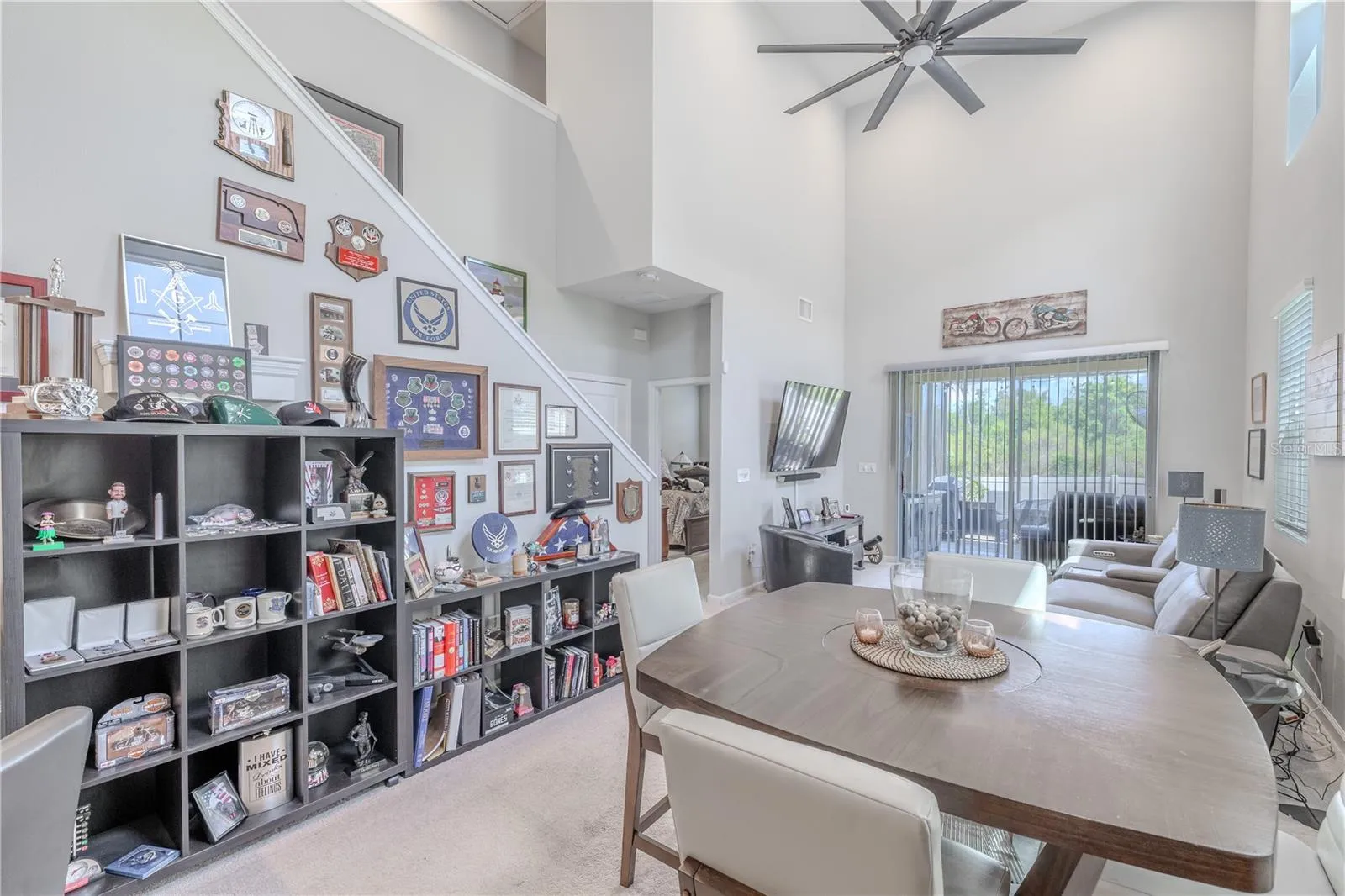 The staircase rises alongside the open living and dining area, where the dramatic ceiling height and rear sliders create a strong sense of space and connection to the screened lanai.