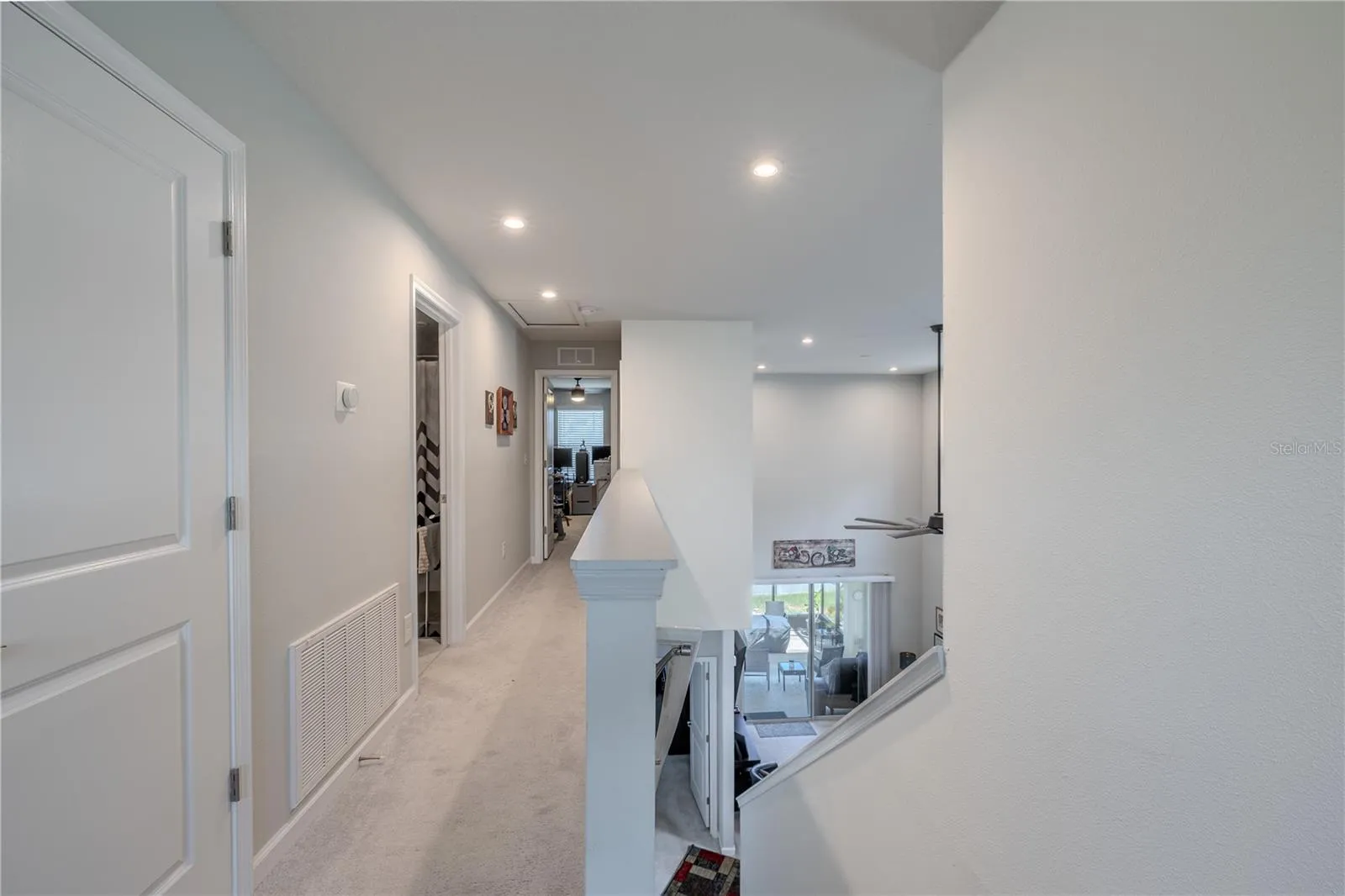 The upstairs hall overlooks the main living area below, with recessed lighting, neutral carpet and an open railing that keeps the second floor feeling connected to the home’s dramatic central space.
