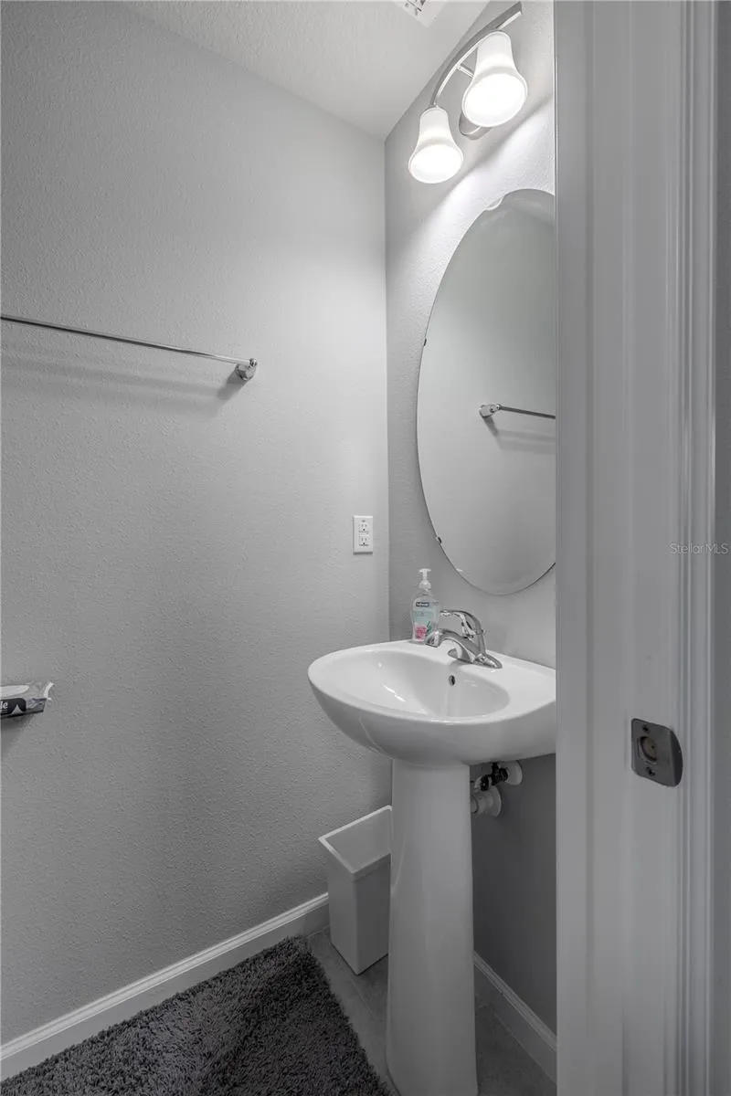 A convenient main-level powder room features a pedestal sink, oval mirror and neutral finishes.