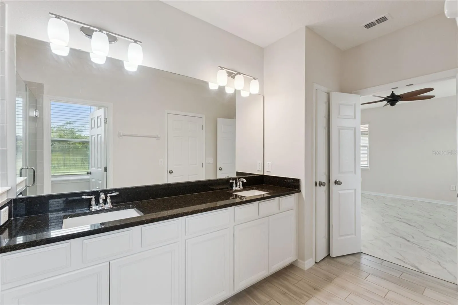2nd Primary Bathroom – Spacious primary bath features an extended dual-sink vanity with dark stone countertop, abundant cabinetry, a large wall mirror, and bright vanity lighting.