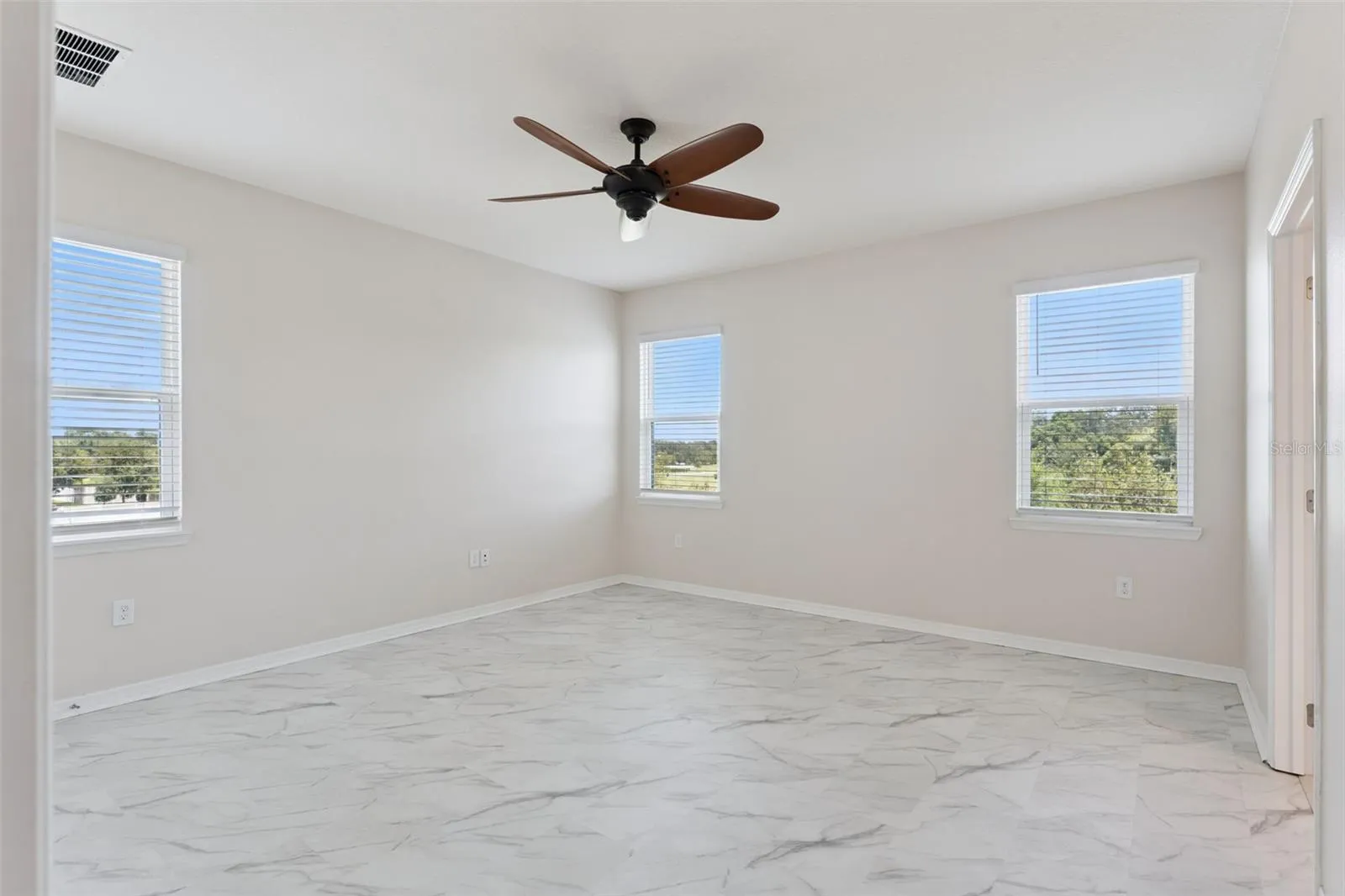 2nd Primary Suite (Upstairs)  – Spacious upstairs primary bedroom with marble-look tile flooring, a ceiling fan, and multiple windows providing abundant natural light.