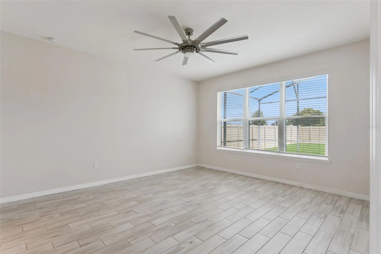 Primary Bedroom – Main-level primary bedroom offers generous proportions, wood-look tile flooring, a statement ceiling fan, and a wide window bringing in abundant natural light.