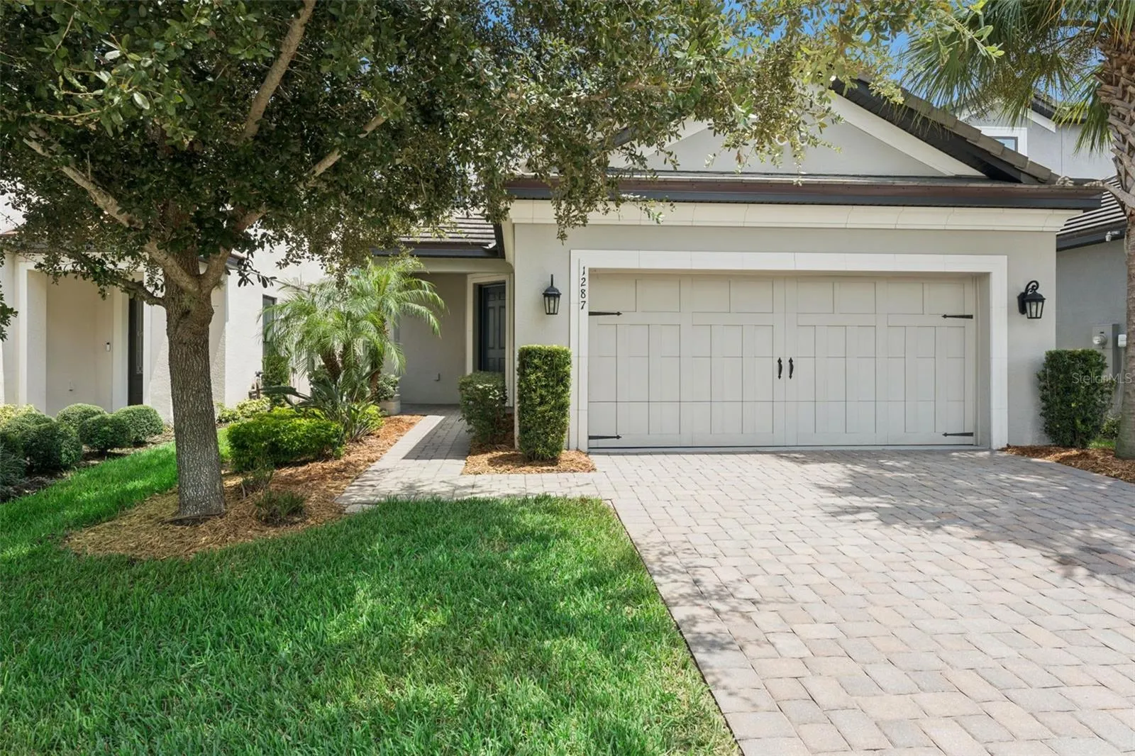 Front Exterior – Welcoming front exterior with mature landscaping, a paver driveway, and a two-car garage with carriage-style detailing.