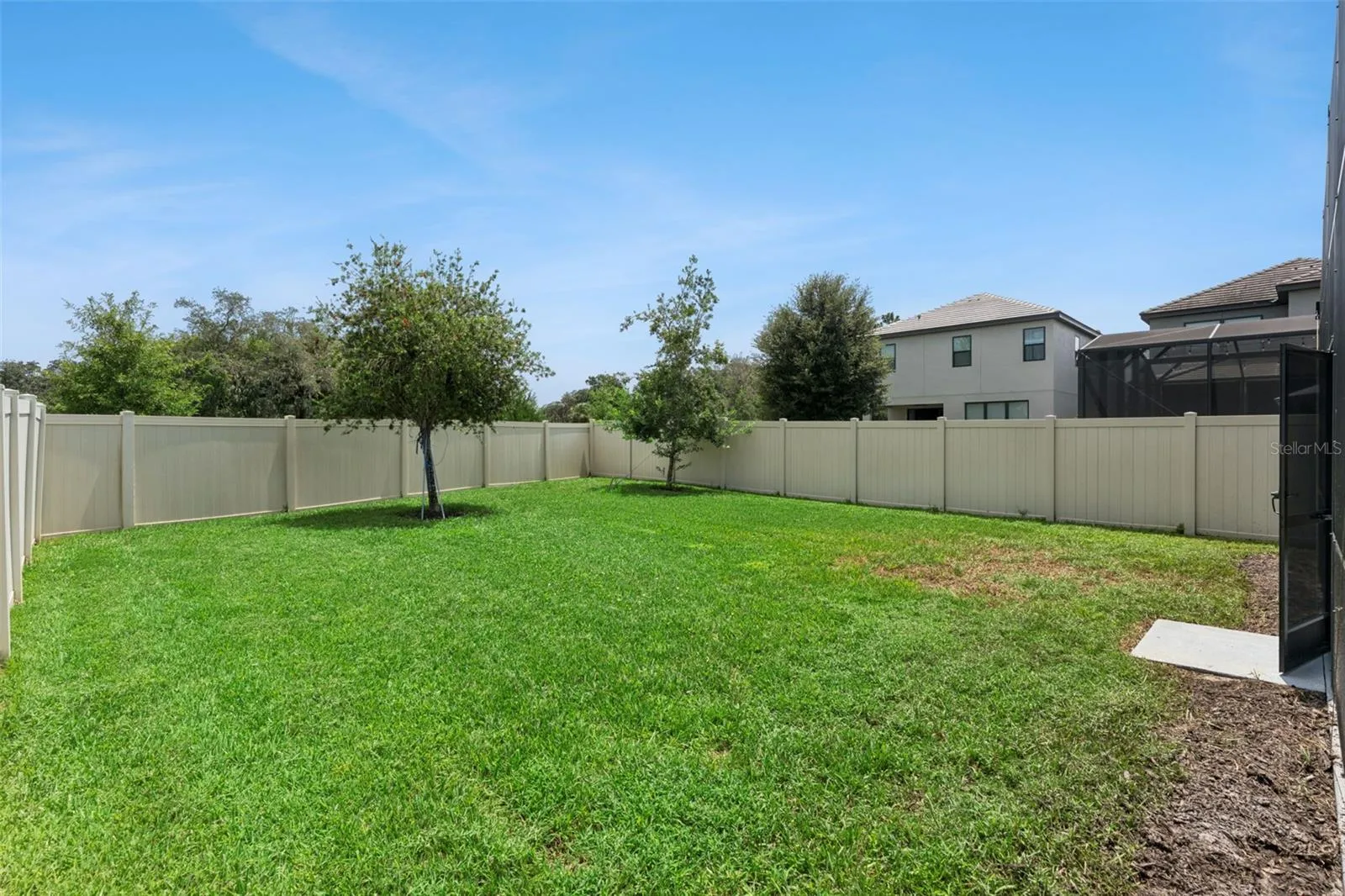 Fenced Backyard – Wide backyard view highlights the open lawn, established trees, and privacy fencing around the property.