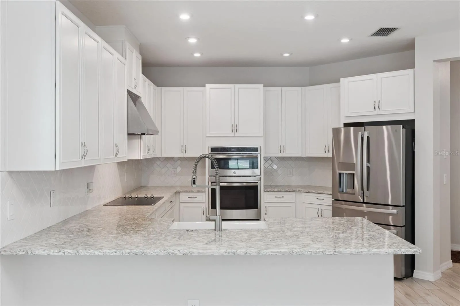 Kitchen – Spacious kitchen features abundant white cabinetry, granite countertops, a classic tile backsplash, stainless steel appliances, double wall ovens, and a generous peninsula with farmhouse-style sink and statement faucet.