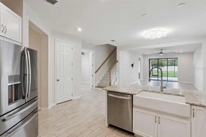 Kitchen & Open Living Area – Open-concept kitchen connects seamlessly with the main living area and features granite countertops, a farmhouse-style sink, stainless steel appliances, and a large peninsula overlooking the room and screened patio beyond.
