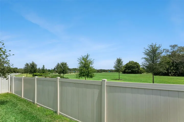 Fenced Backyard – The backyard enjoys an open outlook beyond the rear fence, with expansive maintained green space and mature trees in view.