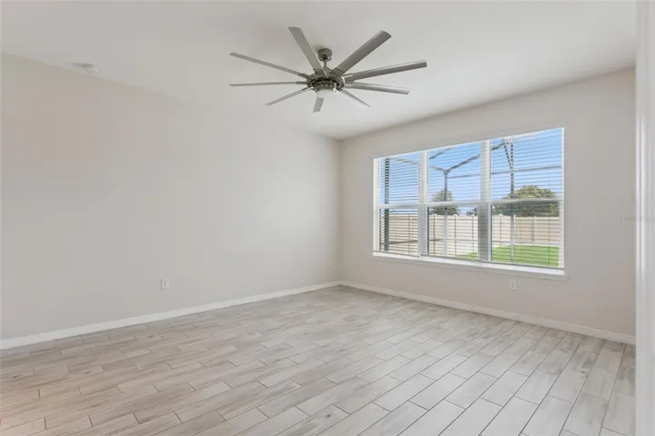 Primary Bedroom – Main-level primary bedroom offers generous proportions, wood-look tile flooring, a statement ceiling fan, and a wide window bringing in abundant natural light.