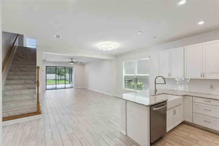 Kitchen & Main Living Area – Wide view highlights the home's open layout, with the kitchen flowing into the spacious living area and sliding glass doors extending the sightline to the screened patio and backyard.