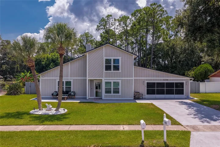 Charming two-story home featuring light exterior siding, a manicured green lawn, and mature palm trees framing the front yard. The driveway leads to an attached garage alongside a paved walkway to the entrance.