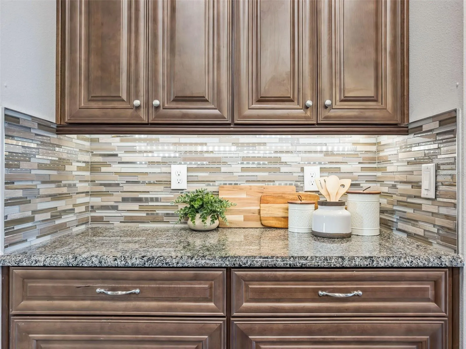 Kitchen detail with granite countertops, solid wood cabinetry, and glass mosaic tile backsplash.