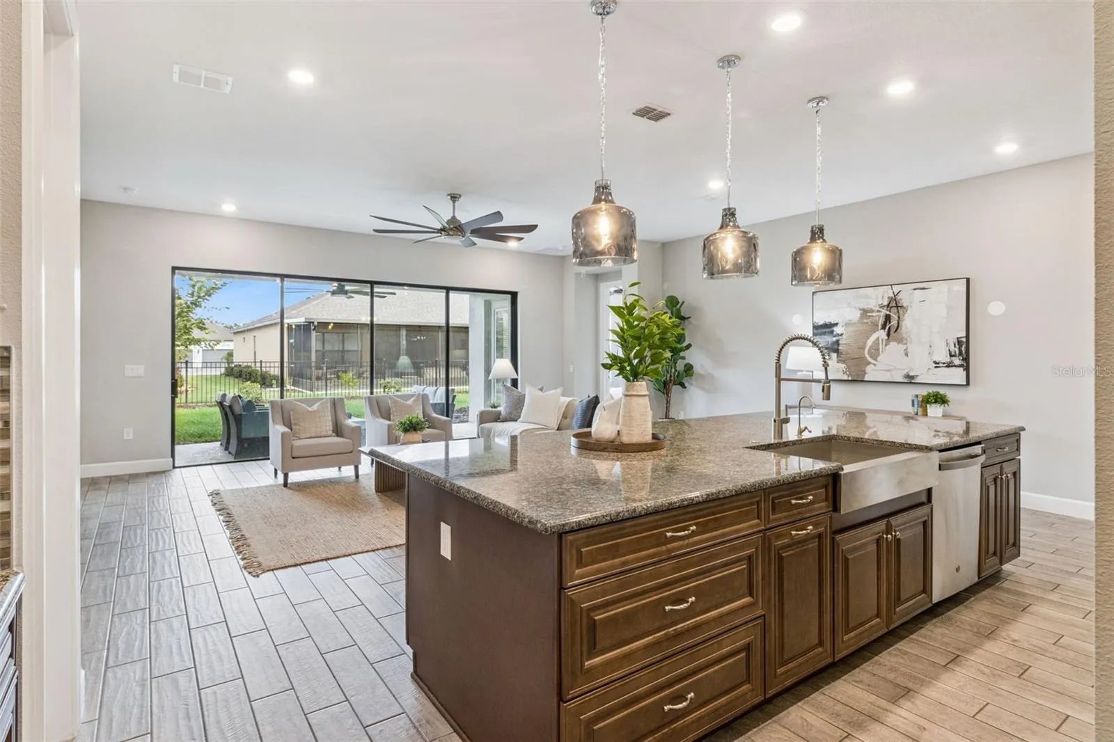 Kitchen island with pendant lights open to the family room and patio beyond.