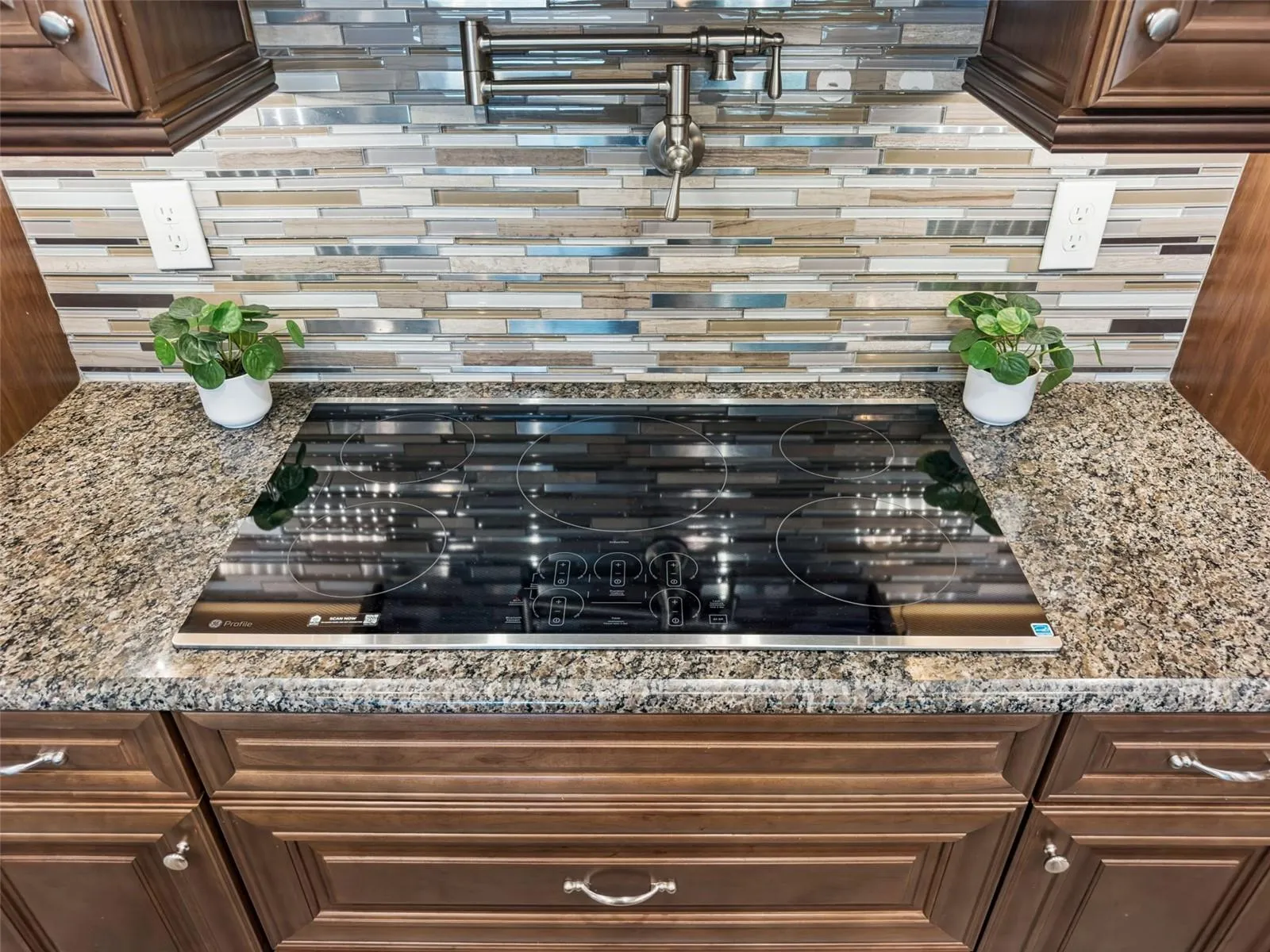 Cooktop set in granite counters with a glass mosaic tile backsplash.