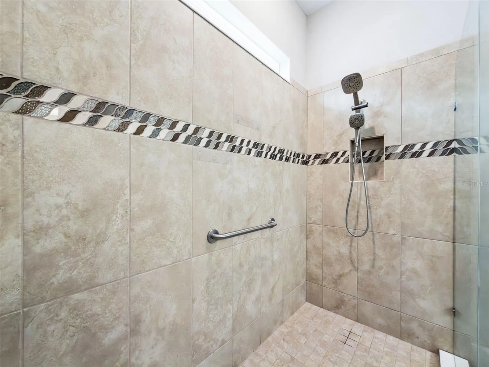 Oversized tiled walk in shower with decorative accent band and glass door.