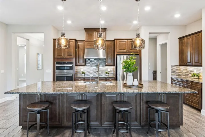 Centrally located kitchen with granite island, breakfast bar seating, solid wood cabinetry, and stainless steel appliances.