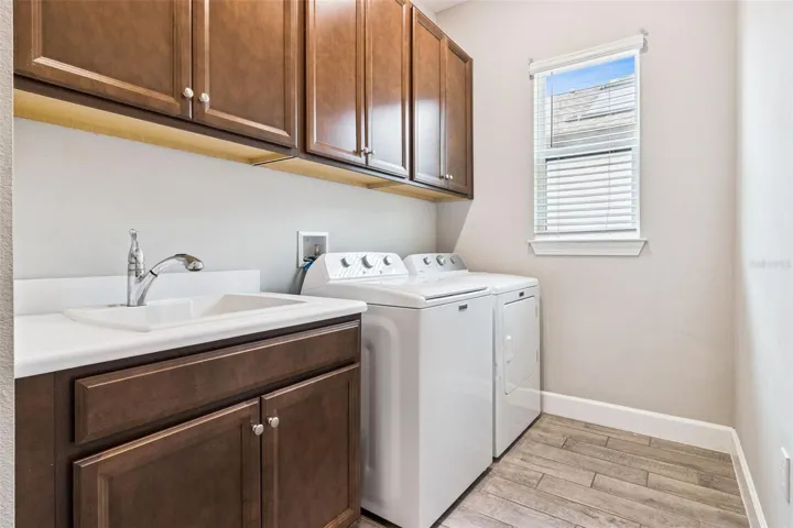 Indoor laundry room with upper cabinets, sink, and washer and dryer.