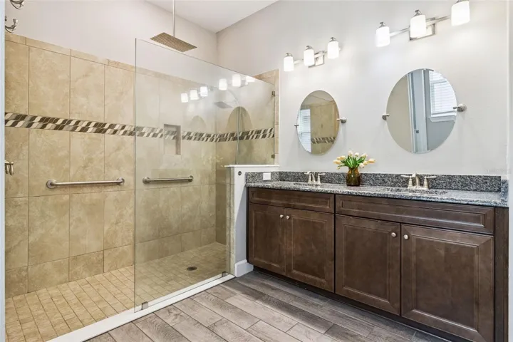 First primary bathroom with dual sink vanity, granite counters, and glass enclosed walk in shower.