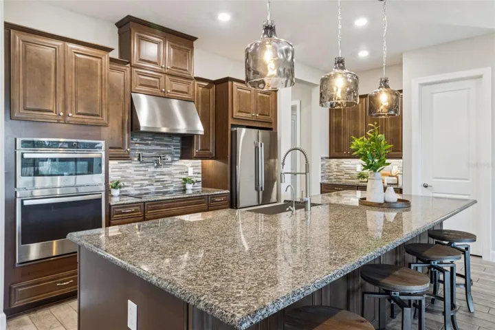 Kitchen with granite counters, tile backsplash, double wall ovens, solid wood cabinetry, and stainless steel appliances.