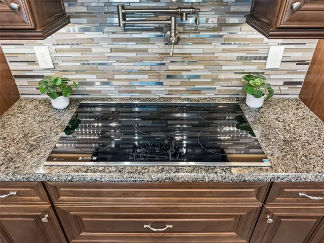 Cooktop set in granite counters with a glass mosaic tile backsplash.