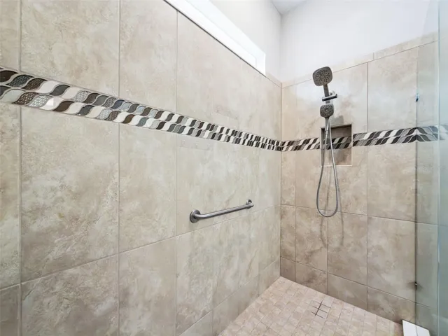 Oversized tiled walk in shower with decorative accent band and glass door.