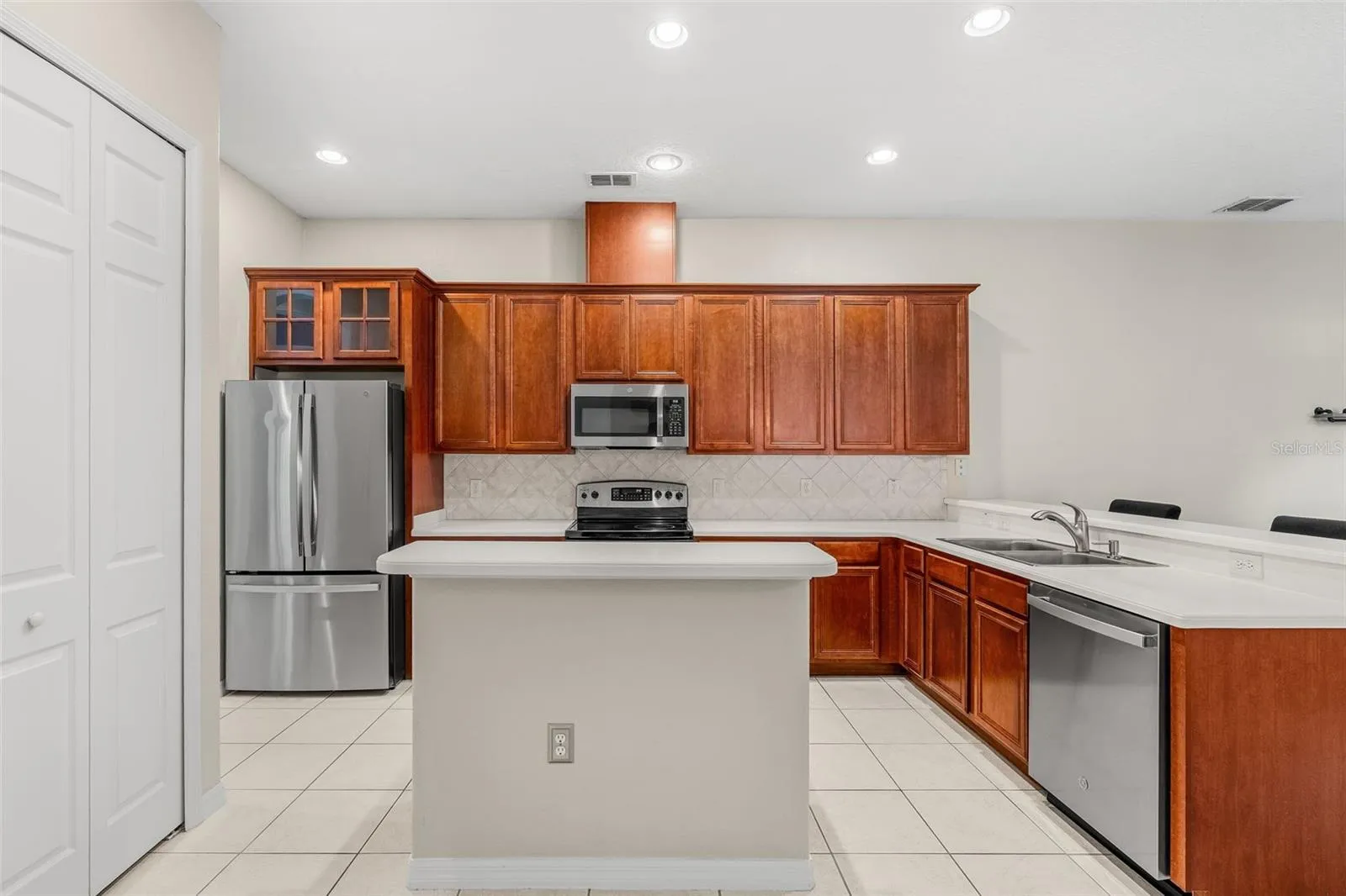 The spacious Kitchen offers ABUNDANT CABINETRY and counter space, a large ISLAND WITH BREAKFAST BAR, sleek backsplash, TWO PANTRY CLOSETS and stainless steel appliances including a NEW REFRIGERATOR (2026), NEW DISHWASHER (2026) and NEW MICROWAVE (2025).