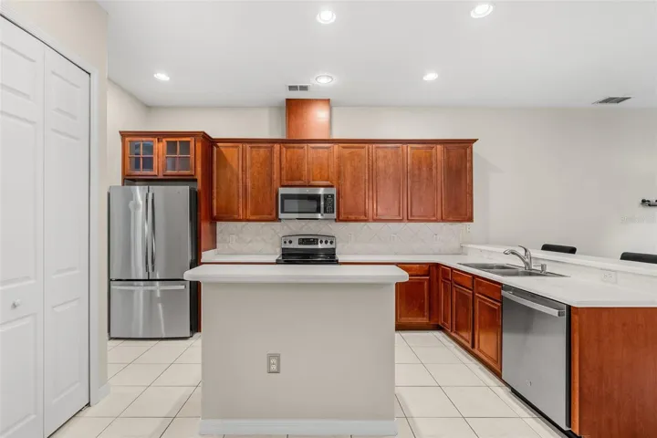 The spacious Kitchen offers ABUNDANT CABINETRY and counter space, a large ISLAND WITH BREAKFAST BAR, sleek backsplash, TWO PANTRY CLOSETS and stainless steel appliances including a NEW REFRIGERATOR (2026), NEW DISHWASHER (2026) and NEW MICROWAVE (2025).